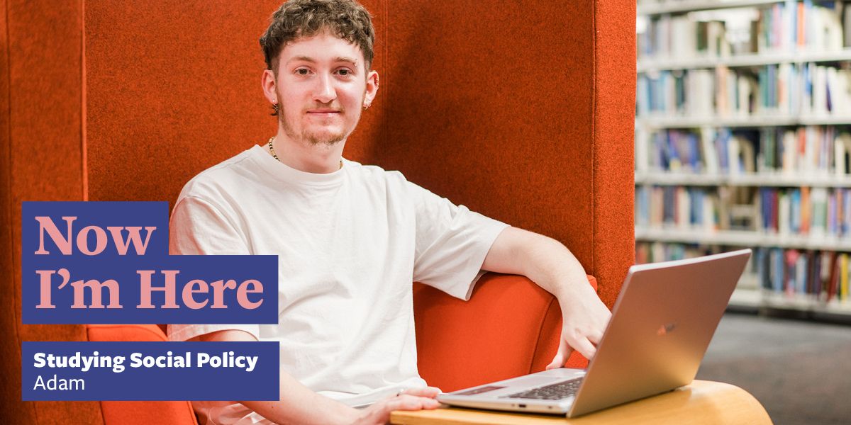 A student sat in a bright orange study booth in a library with their laptop open on a table in front of them and a shelf of books in the background. Text says: Now I'm Here studying social policy, Adam