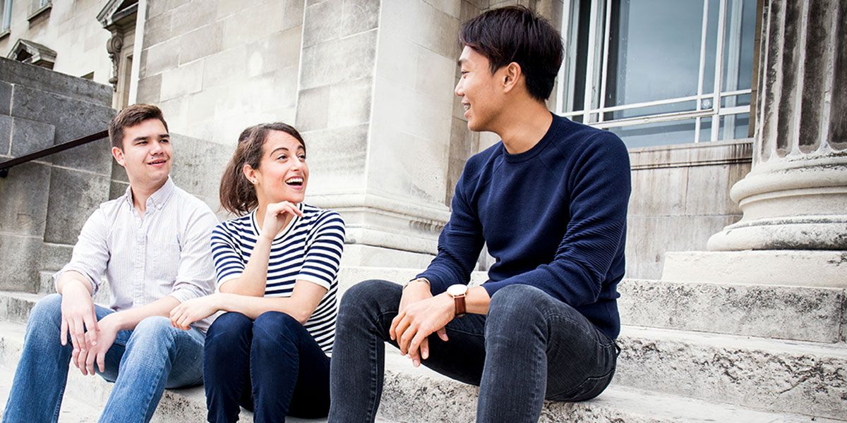 Three students sat on steps in front of the Parkinson Building, chatting and smiling