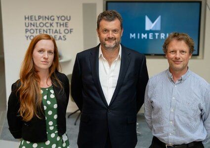Three people stood facing the camera. One woman on the left, one man in the middle and one man on the right. Behind them is the Mimetrik logo on a tv screen.