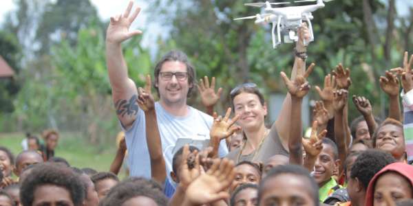 Joanna Lester stands in a crowd of children in Papua New Guinea holding a drone in the air