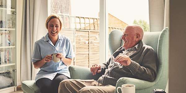 A care-taker and a resident having a conversation and laughing in an elderly care home.