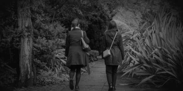 Two young women walk towards some shrubbery in a park
