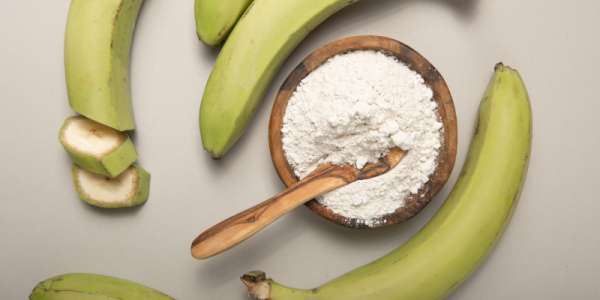 A handful of slightly green bananas placed around a wooden bowl of flour, with a wooden spoon in the flour.