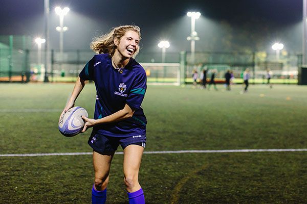 A student on a floodlit rugby pitch throwing a rugby ball