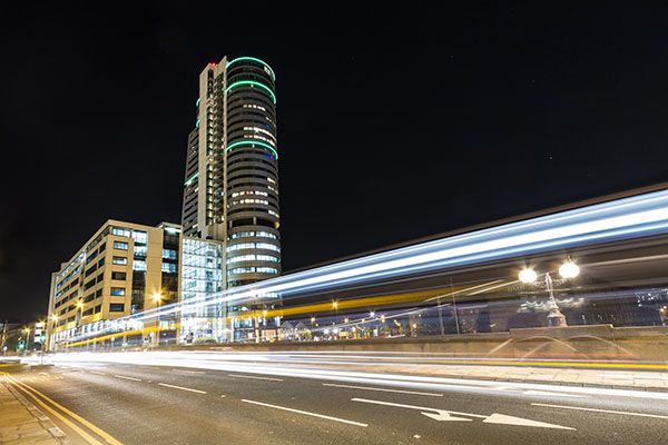 Bridgewater Place, a tall commercial and residential building in South Leeds, lit up at night. Light trails from cars cross the picture diagonally in the foreground.
