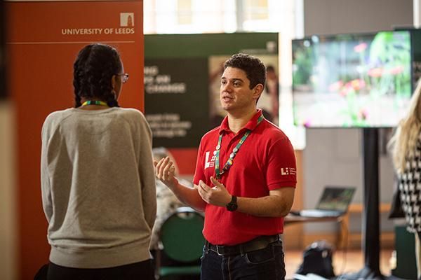 A University of Leeds representative wearing a red shirt is speaking to a prospective student at an Open Day.