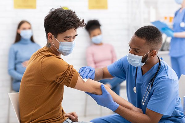 A man receives a vaccination from a male medical professional dressed in blue scrubs