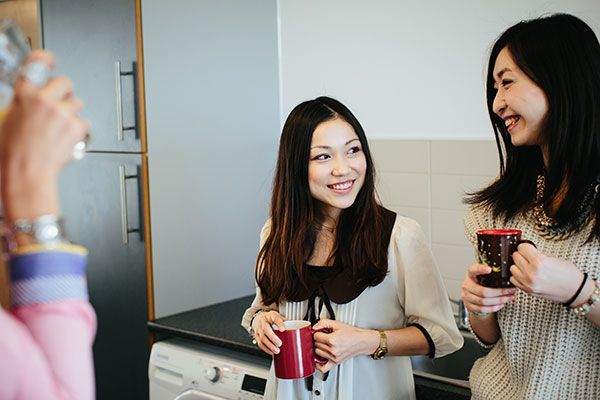 Two female students standing up, talking in a university hall of residence kitchen.