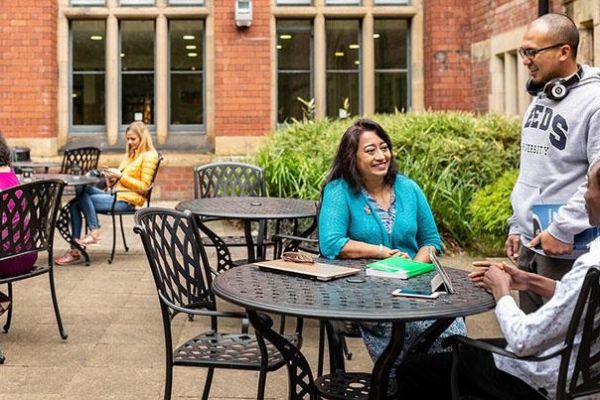 Three postgraduate researchers chat in courtyard cafe on campus