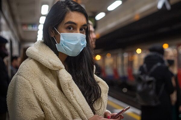 Woman, wearing a mask, on an Underground platform, waiting for a train
