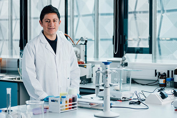 Postgraduate researcher Vicente Merida in a white lab coat stands in an engineering laboratory.