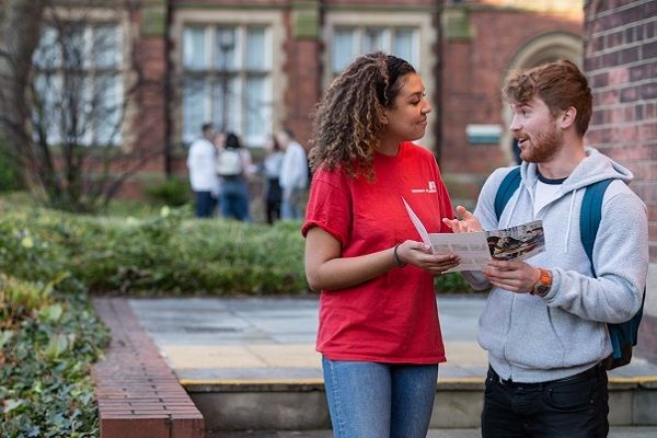 A visitor chatting to an open day ambassador on campus. They are looking at a leaflet