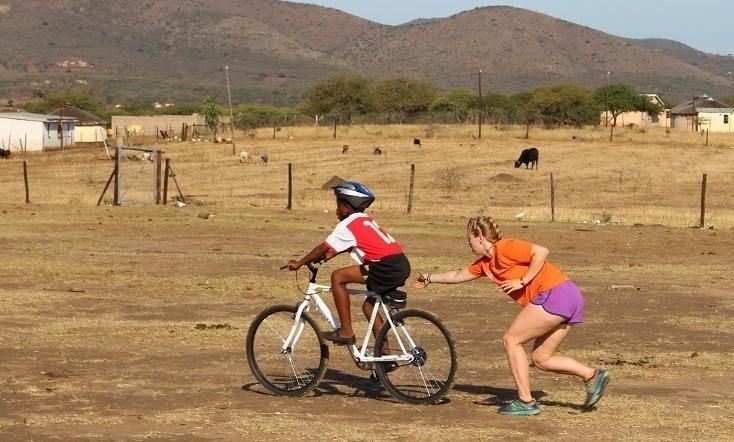 A University student teaches a young person in South Africa to ride a bike to get to school more quickly and easily