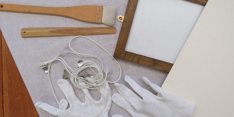 Artists' equipment including two white gloves, a brown photo frame, white paper, white string and a paintbrush.