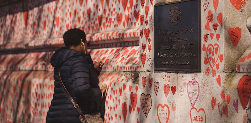 A person adds a name to the National COVID memorial wall: a white stone wall with red hearts and drawn on.