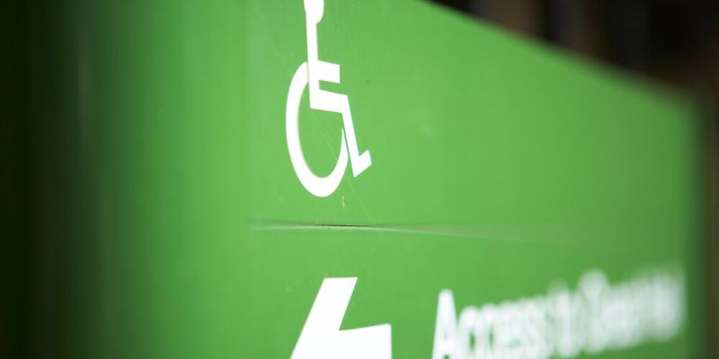 A green sign with a wheelchair user symbol, an arrow and blurred writing