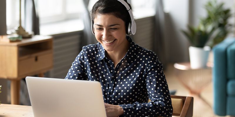 A student wearing headphones smiles while working at a laptop