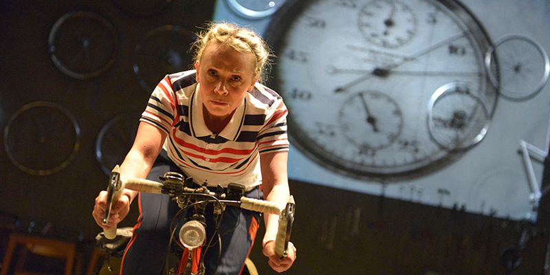 Person rides a bike with clocks in the background as part of the Beryl theatre production
