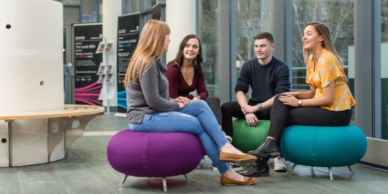 Four students talking in the Business School foyer.