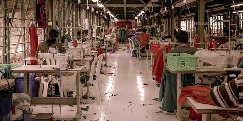 People sitting making clothes in a clothing factory.