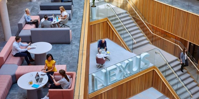 Looking down on an open area of the Nexus building with groups of adults sitting and working together.