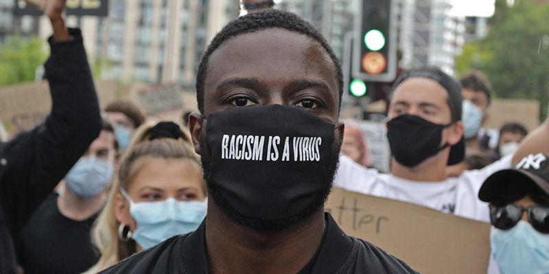A man wearing a mask that says 'Racism is a Virus'.