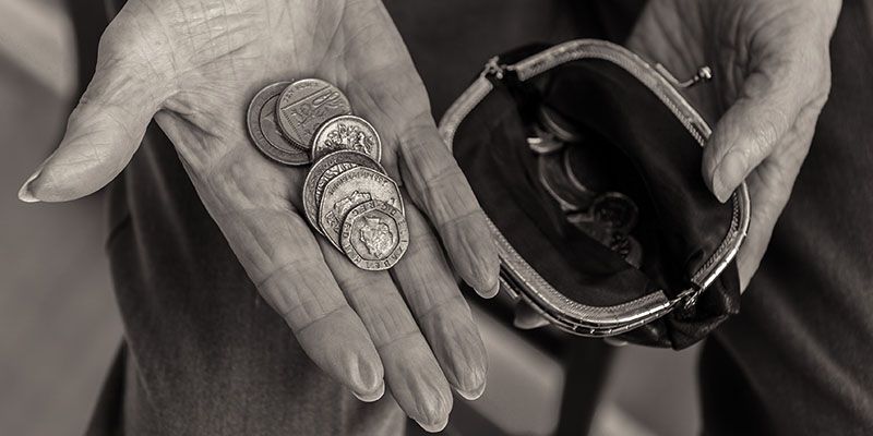 Close-up of an elderly person's hands, with one holding British coins, and another holding a coin purse, to depict poverty in the UK