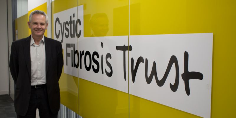 Dr Keith Brownlee stands before a Cystic Fibrosis Trust banner smiling at the camera