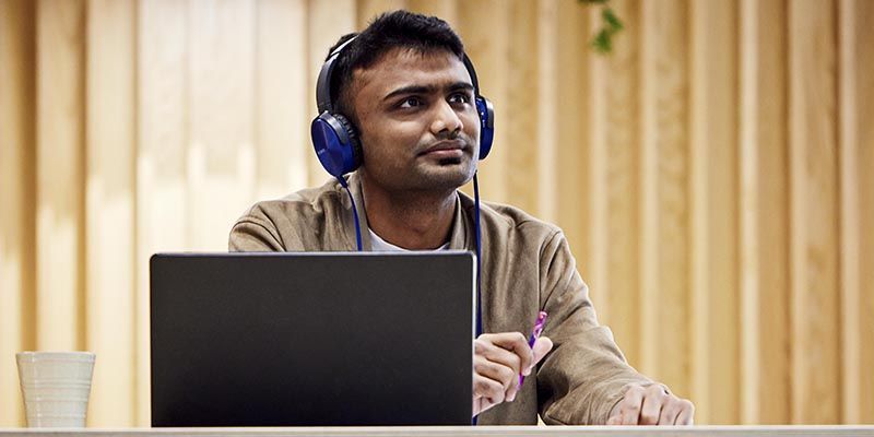 A student wearing headphones and using a laptop in a bright open public space.