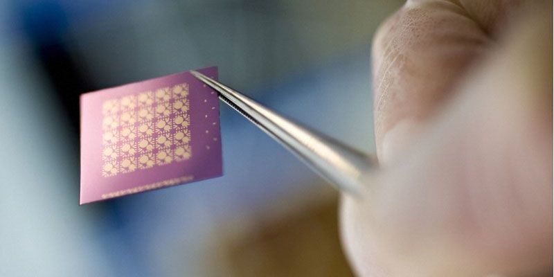 A patterned semiconductor microchip held in a pair of tweezers