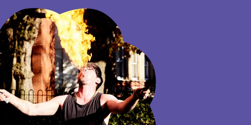 Photo of a circus performer breathing fire within a cloud-shaped purple graphic.
