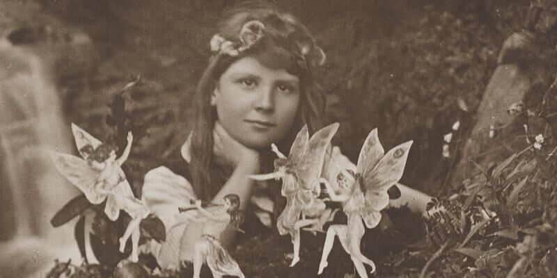 A black and white image of a young person with fairies dancing around them