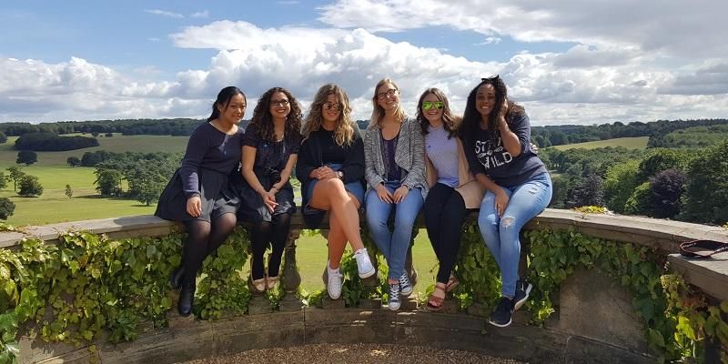 6 Leeds International Summer School students sat on a wall at Harewood House on a sunny day in 2016