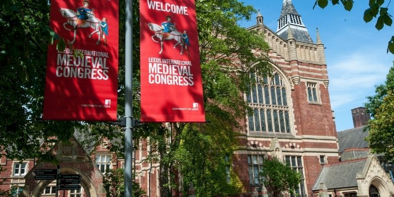 A red banner in front of The Great Hall with text that says 'Welcome Leeds International Medieval Congress'