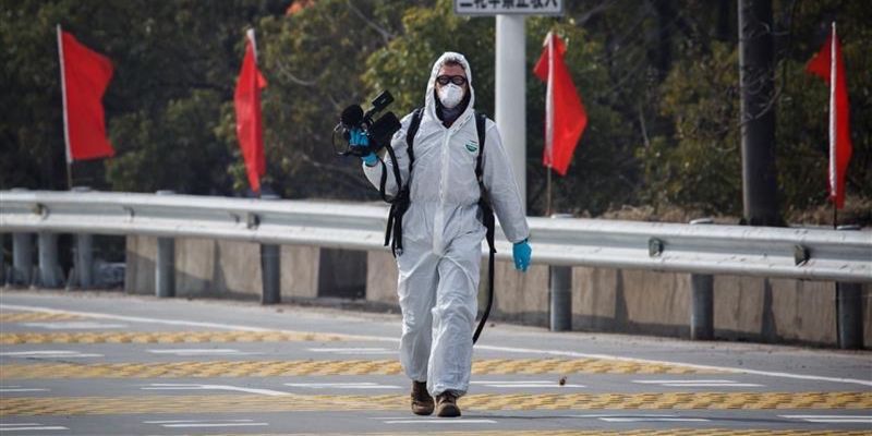 Leeds alumnus Martin Pollard in a face mask and hazmat suit holding a camera while reporting on the COVID-19 pandemic in China.