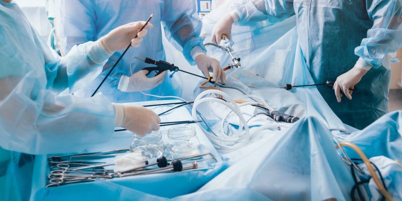 three surgeons in gowns and gloves seen from the shoulders down, using medical implements to perform an operation