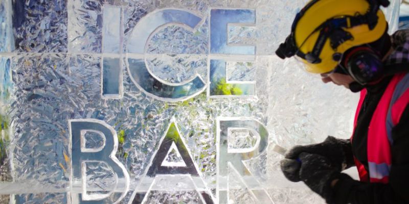 A person in protective clothing carving the words ice bar into ice.