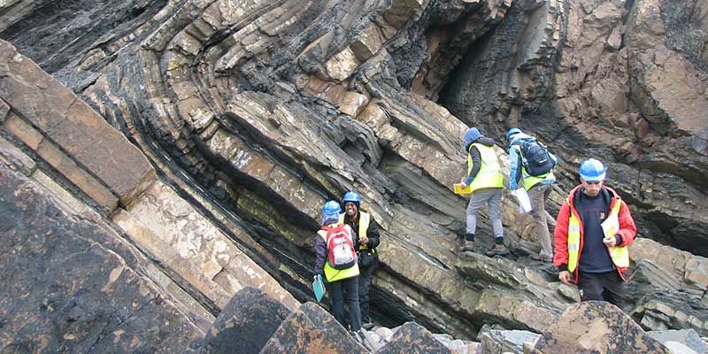 Researchers wearing hard hats work at a fault line.