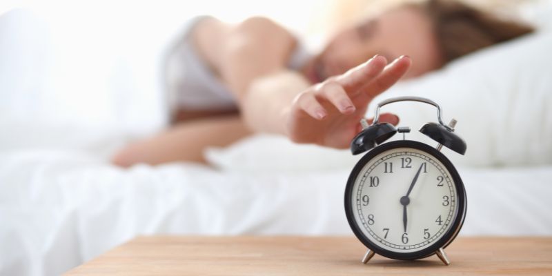 Young sleeping person reaching for an alarm clock in their bedroom