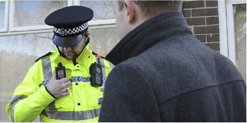 Picture shows a police officer with a body worn camera on his tunic talking to a witness
