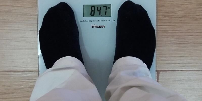 The image shows someone standing on a set of weighing scales. You can only see them from their knees down.
