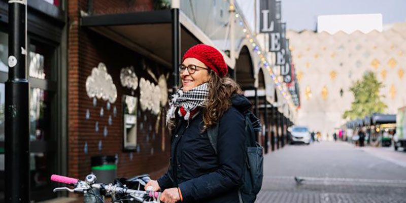 Professor Sara Gonzalez, wearing winter coat, scarf and a red hat, parks a bike outside Kirkgate Market.