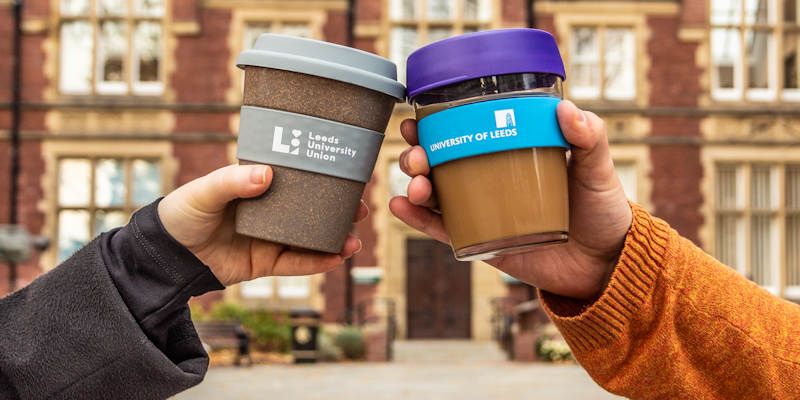 Two hands holding University of Leeds reusable coffee cups.