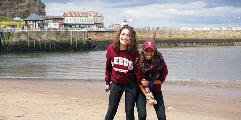 Two smiling students on Whitby beach in North Yorkshire