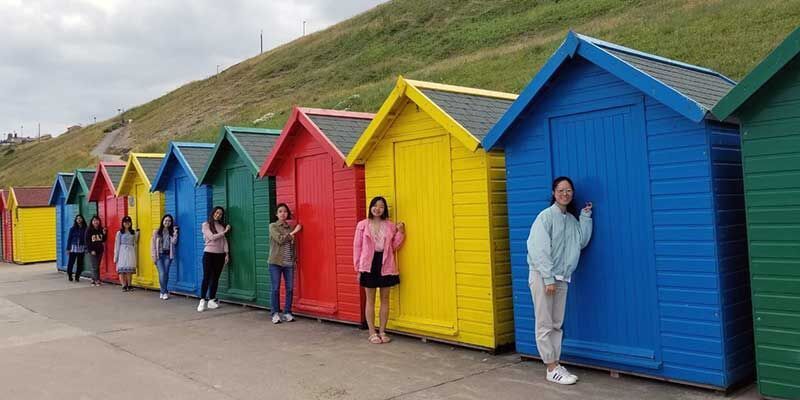 Students stood in front of the brightly coloured beach huts in Whitby, Yorkshire