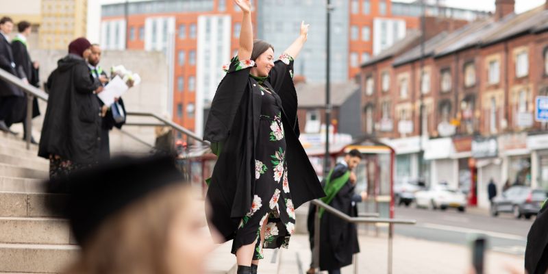 Graduating student stands with arms raised in celebration on the Parkinson Steps