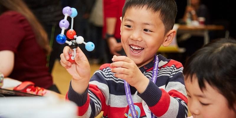 A child smiling and playing with a model of molecules at Be Curious Live.