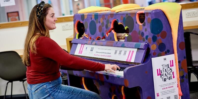 A woman seated playing a piano painted bright colours