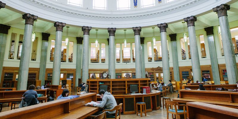 Students working in the Brotherton Library, showing  a traditional interior with wooden furniture, stone columns and domed ceiling