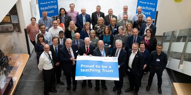 A group of doctors from the University of Leeds and Mid Yorkshire Teaching NHS Trust holding a sign that says proud to be a teaching Trust